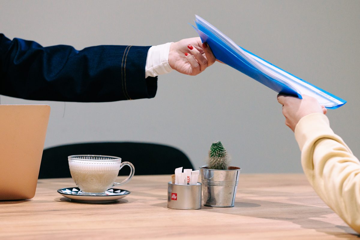 Handing over a blue folder across the table in the meeting room